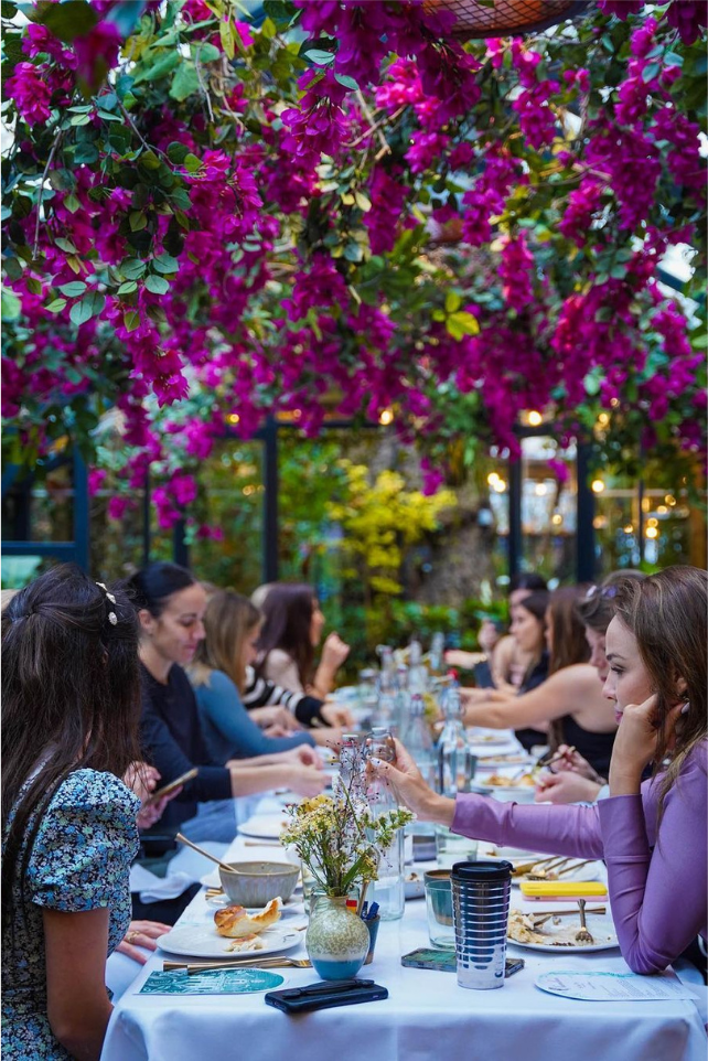 Women gathered at a long table under flowers at the SAÏA Brunch Club